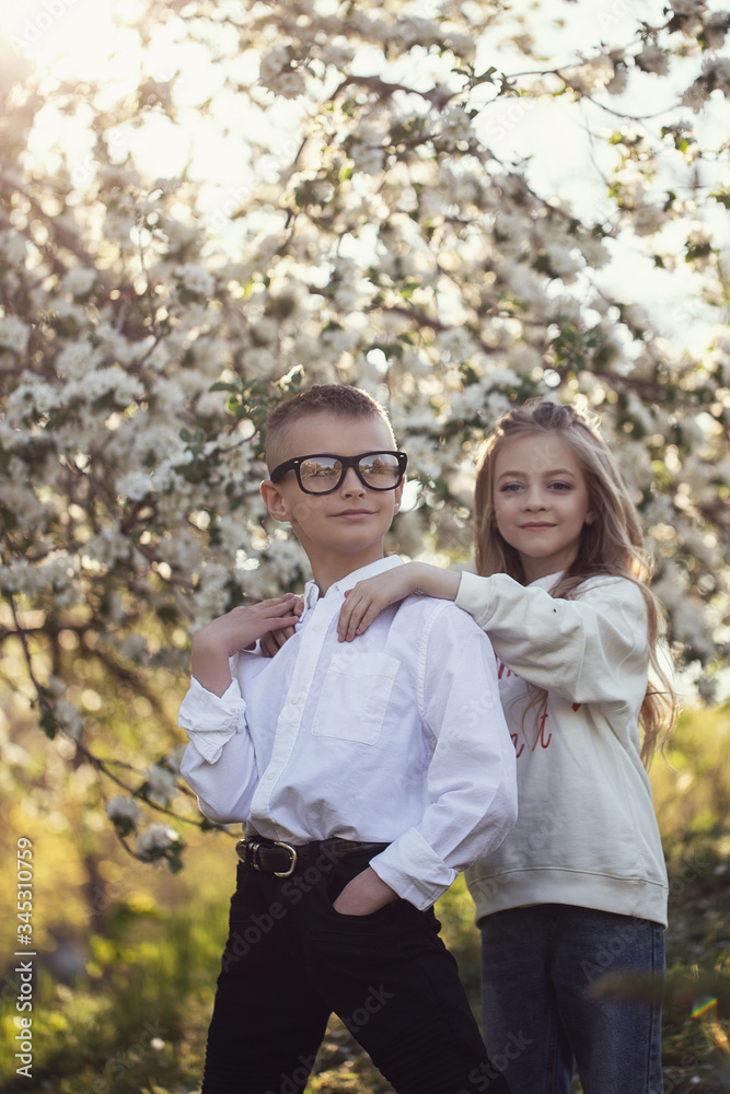 Two little Caucasian children wolk in the park with each other. Brother and sister spend time together.older brother help his younger sister with homework. Stylish clothes,cool glasses and happy faces Two little Caucasian children wolk in the park with each other. Brother and sister spend time together.older brother help his younger sister with homework. Stylish clothes,cool glasses and happy faces