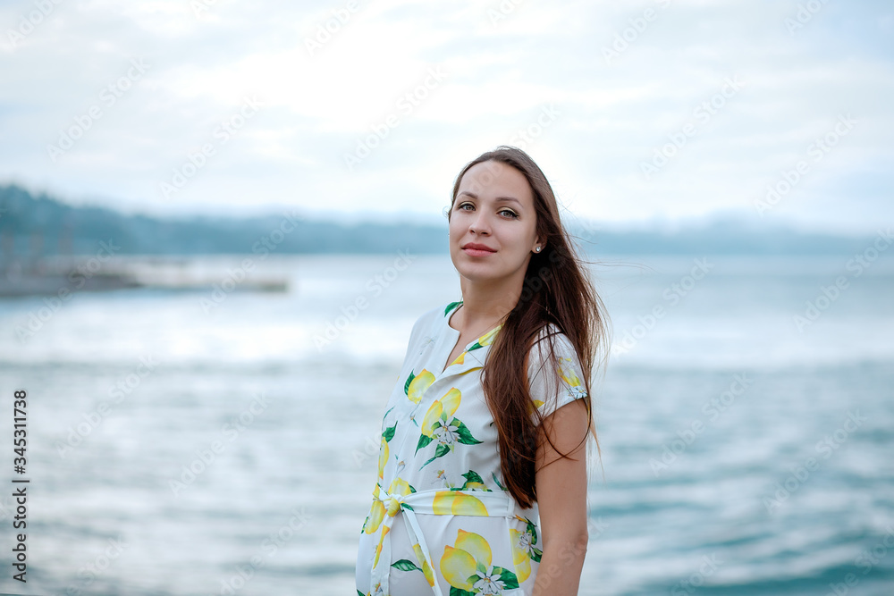 pregnant woman in a dress with lemons stands on the turquoise sea coast looking in frame pregnant woman in a dress with lemons stands on the turquoise sea coast looking in frame