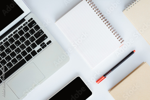 Top view of white office desk with laptop computer, smartphone, notebook and a pen for business and workspace concept