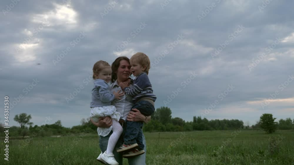 Happy Mother Holding Son and Daughter on Hands in the Field. Slow motion Happy Mother Holding Son and Daughter on Hands in the Field. Slow motion