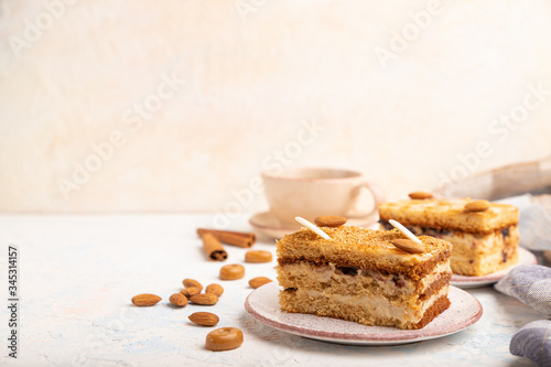 Honey cake with milk cream, caramel, almonds and a cup of coffee on a white concrete background. Side view, copy space, selective focus.