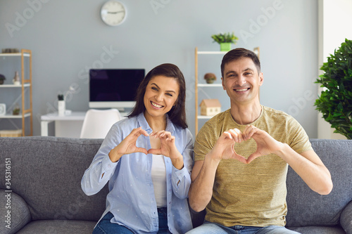 Happy smiling couple holds hands in the shape of a heart welcomes sitting in the house