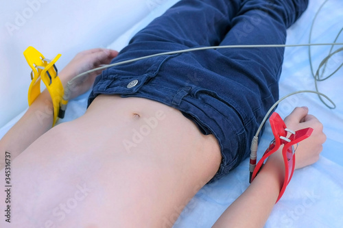 Doctor cardiologist preparing child boy to cardiogram heart procedure, closeup. Woman cardiologist making heart cardiogram for child boy lying on couch, hands closeup. photo