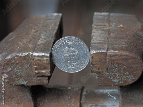 Coin one Tunisian Dinar, clamped in a metal vise, close-up. concept of financial problems and crisis. Pressure on the currency photo