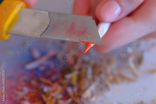 Woman painter artist sharpening orange pencil using sharp knife, hands closeup. Teacher sharpen orange pencil for her students on white table. Preparing to work in art studio. photo