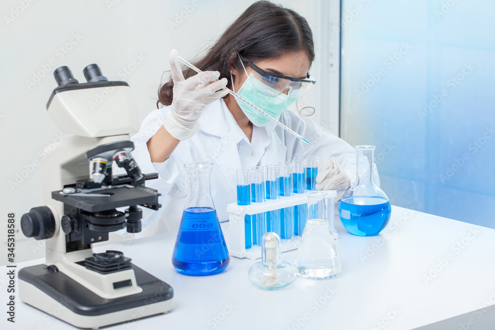 Fototapeta premium medical woman with mask or scientific researcher or scientist working with a microscope and test tubes in a laboratory