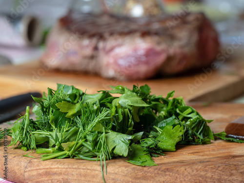 Fresh chopped greens in the foreground and a piece of meat blurred in the background. Concept of food and proper nutrition photo