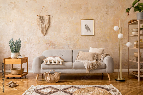 Stylish scandi compostion at living room interior with design gray sofa, wooden coffee table, shelf, cube, carpet, rattan pouf, plants, picture frame, table lamp and elegant accessories in home decor. photo