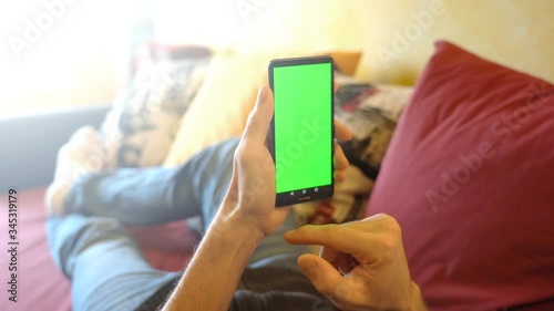 Man at Home Lying on a Couch using Smartphone with Green Mock-up Screen, horizontal scrolling