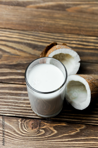 Coconut vegan milk in a glass and coconut broken in half on a dark wooden background