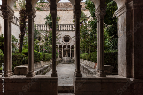 Botanical garden with greenery of the 13th Century Franciscan Monastery cloister in the Old Town of Dubrovnik, Dalmatia, Croatia. Romanesque gothic style. Decorative columns and a fountain photo