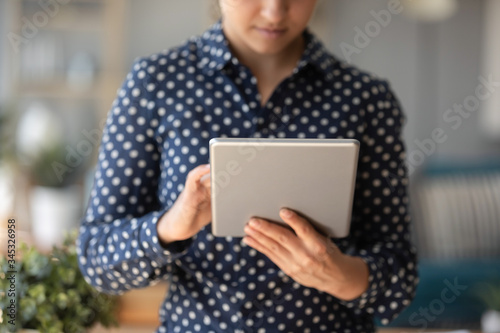 Cropped image close up concentrated young indian girl using digital computer tablet, web surfing internet, searching information. Millennial hindu woman chatting with friends in social network.