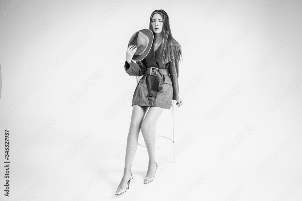 An attractive young girl, a model who looks to the side and straightens her hair in a gray jacket and hat, is sitting on a chair. Men's style clothing. isolated on a white background. Selective focus