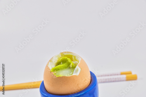œuf à la coque recette japonaise avec de la sauce wasabi dans l’œuf et des baguettes chinoises coquetier bleu
