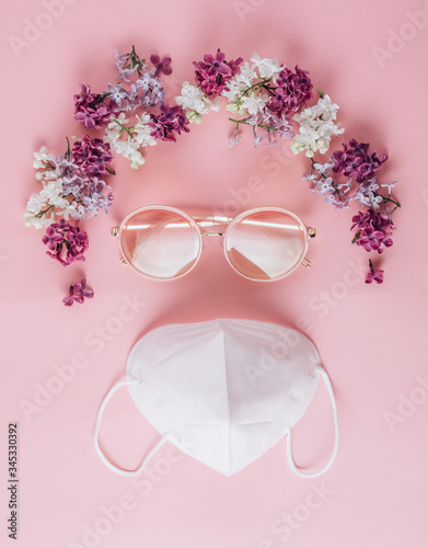 Poker face and keep positive) White KN95 mask with sunglasses and flowers in the shape of hair on pink background. Coronavirus Covid-19 quarantin concept. Top view. photo