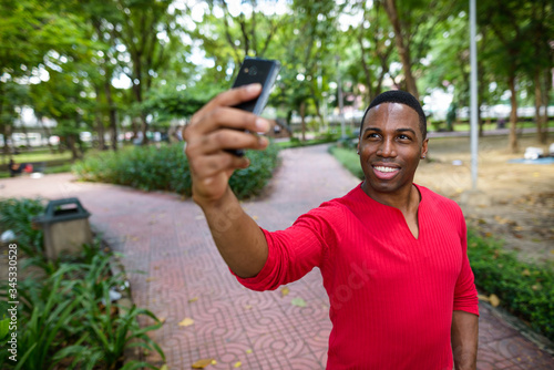 Happy young handsome African man taking selfie at the park © Ranta Images