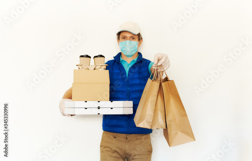 Delivery during quarantine. Courier in protective mask and gloves holding cardboard boxes reaching out hand with paper bags for takeaway food to clients. Takeout meal, online order, deivery to home photo