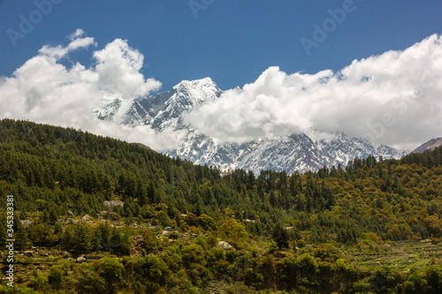 A Himalayan landscape with the snow covered Nilgiri North mountain towering over pristine, green alpine forests on the Annapurna Circuit in Nepal.