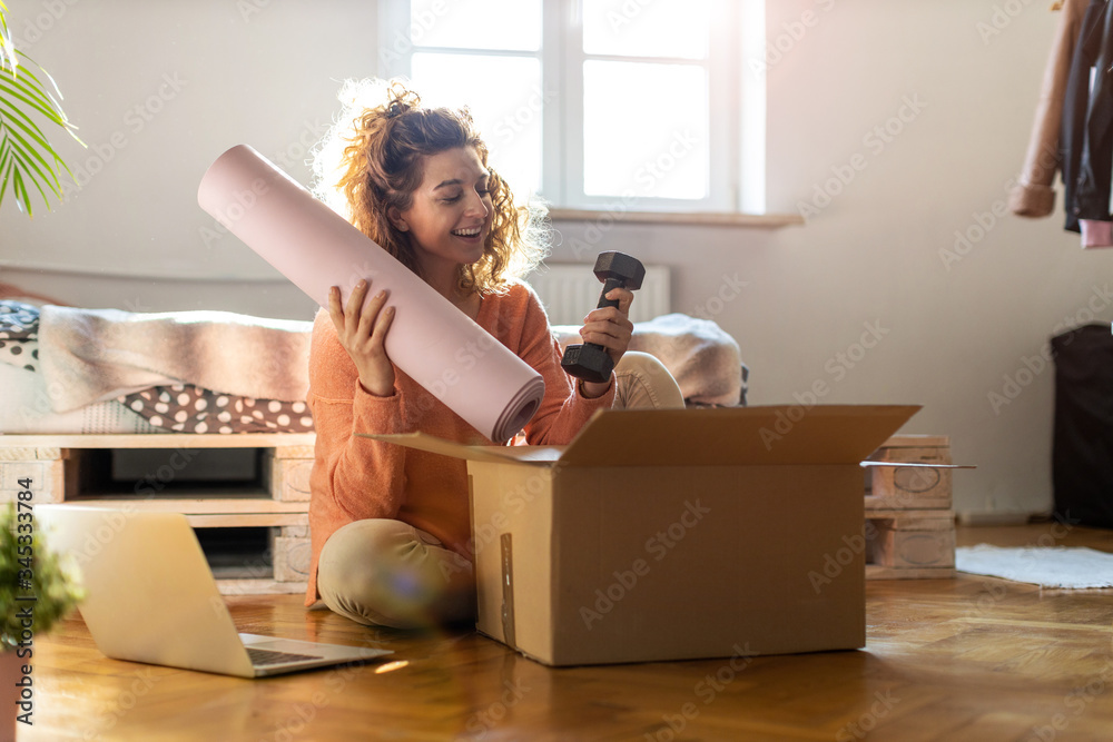 Woman unpacking box with workout equipment at home 
 - obrazy, fototapety, plakaty 