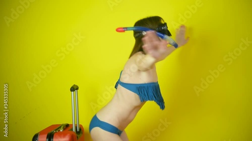 Girl in a swimming mask pretends to swim in the studio isolated on a yellow background. Happy joyful girl dreaming about active summer vacation