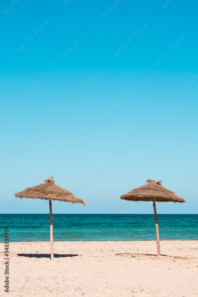 Two beach umbrellas on the sandy beach at sunny day