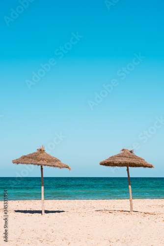 Two beach umbrellas on the sandy beach at sunny day