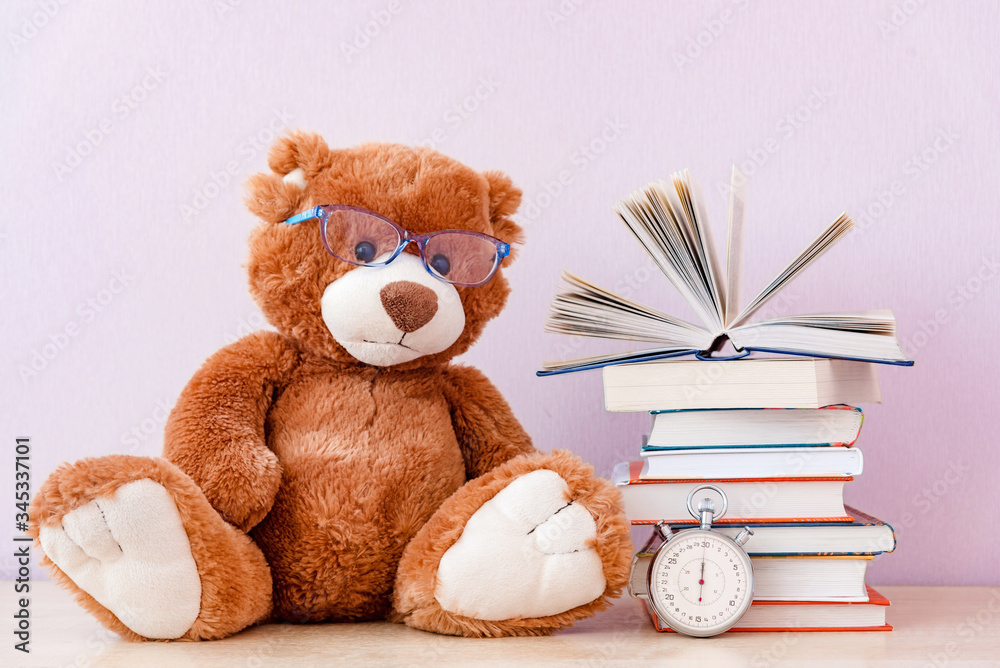 Soft stuffed toy Teddy bear with glasses, a stack of books and a stopwatch. Education concept, reading speed Soft stuffed toy Teddy bear with glasses, a stack of books and a stopwatch. Education concept, reading speed