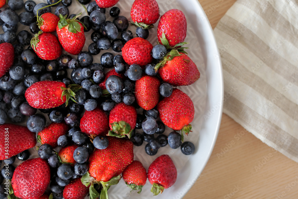 Fresh juicy ripe berries - Blueberries and strawberry оn the white plate on a table background. Top view and copy space. Healthy food concept. Eating lifestyle Fresh juicy ripe berries - Blueberries and strawberry оn the white plate on a table background. Top view and copy space. Healthy food concept. Eating lifestyle