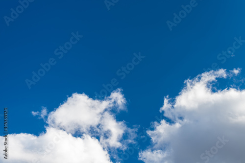 Sunlit blue sky background with copy space and group of white precipitation clouds. Scenic natural view on dramatic airy cloudscape and flowing puffy cumulus. Ecosystem, water cycle or climate change.