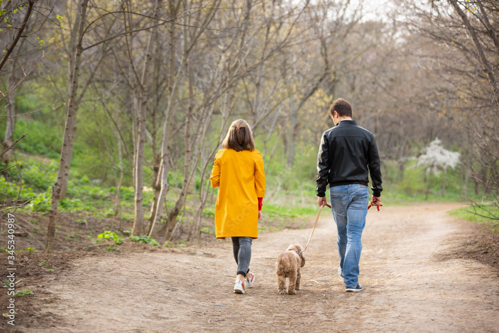 Fototapeta premium Young couple walking with a dog on a trail in a forest. Woman in a yellow coat looking at the camera