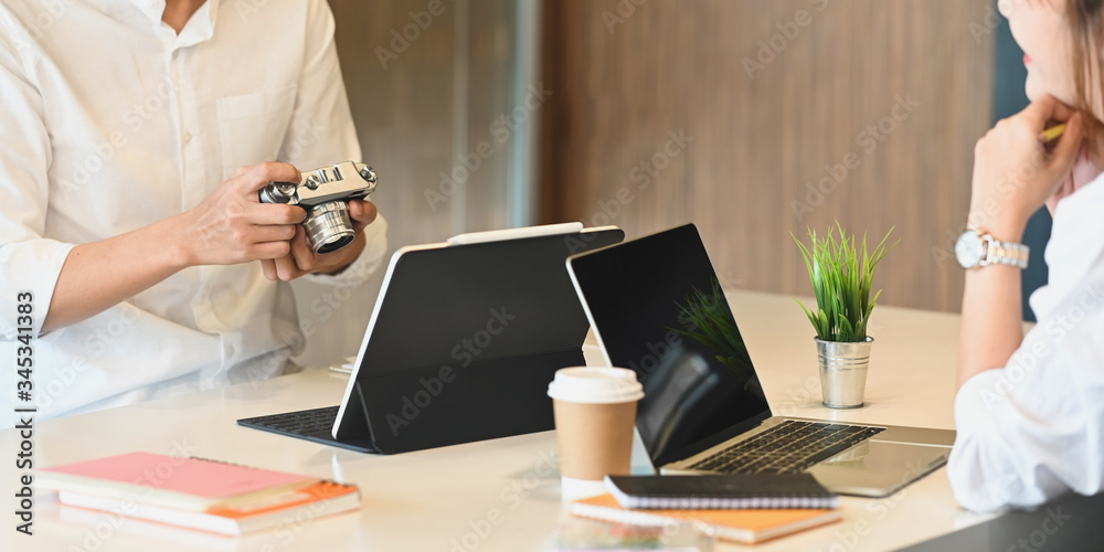 Fototapeta premium Closeup graphic designer team working together with computer laptop and tablet at the wooden working desk over comfortable sitting room as background.