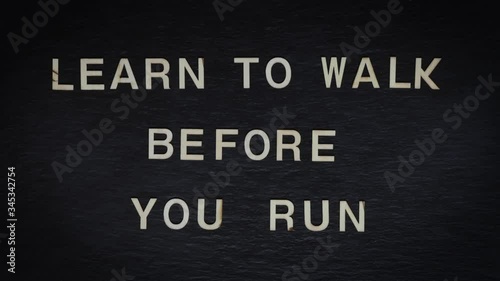 Stop motion of wooden letters writing LEARN TO WALK BEFORE YOU RUN on slate background