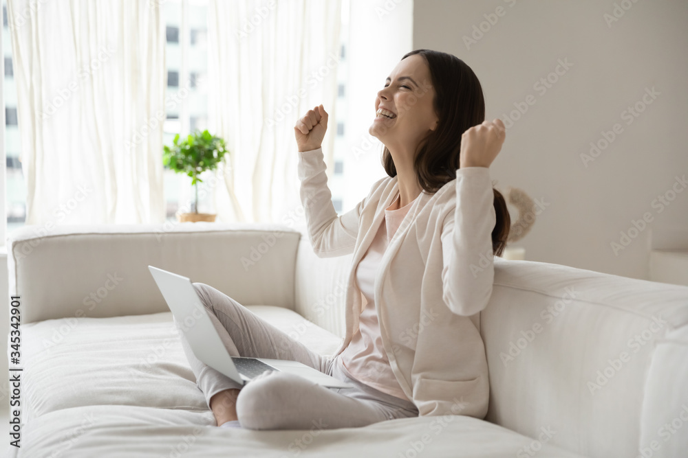 Overjoyed millennial girl sit on sofa ta home feel excited euphoric winning online lottery on laptop, happy young Caucasian woman triumph read good news on internet, get promotion letter on computer Overjoyed millennial girl sit on sofa ta home feel excited euphoric winning online lottery on laptop, happy young Caucasian woman triumph read good news on internet, get promotion letter on computer