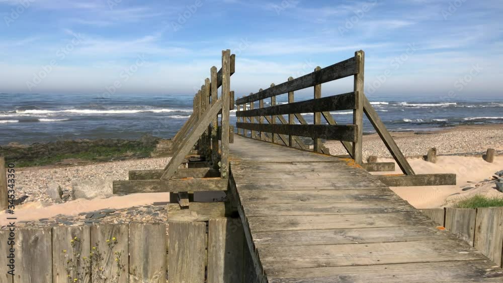 Wooden bridge to the beach in Esposende, Portugal. Sea, beach boulders, pebble shore and waves in the morning. Wooden bridge to the beach in Esposende, Portugal. Sea, beach boulders, pebble shore and waves in the morning.