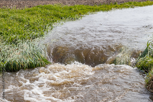 Water flowing in farm field waterway after heavy rain and storms caused flooding. Concept of soil erosion, water runoff control and management