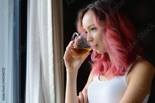 Face of beautiful woman with pink hair drinking tea and looking out the window