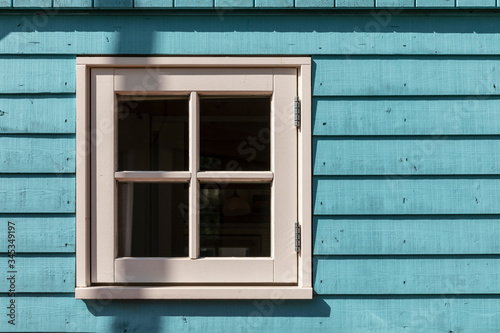 A small window of a tiny house with a white frame and light blue colored hard wooden facade consisting out of panels on a sunny day. Horizontal shot