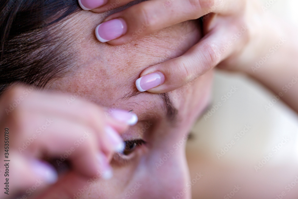 A new life in a pandemic, Young woman, plucking her eyebrows at home, macro A new life in a pandemic, Young woman, plucking her eyebrows at home, macro