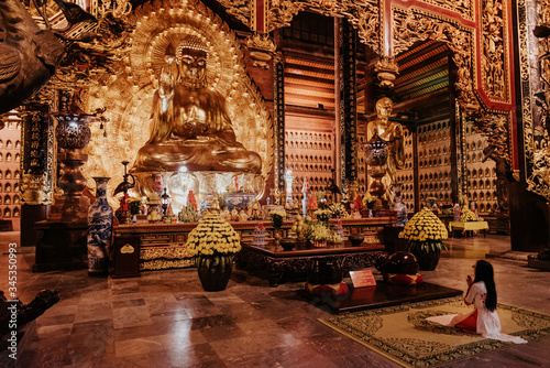 Buddhist girl praying in front of a golden buddha in Bái Đính Temple in Tam Coc, Vietnam