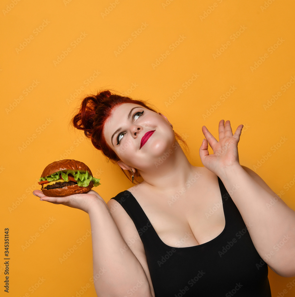 Happy overweight fat woman happy hold big burger cheeseburger sandwich. Girl on diet dieting. Healthy eating fast food concept Happy overweight fat woman happy hold big burger cheeseburger sandwich. Girl on diet dieting. Healthy eating fast food concept