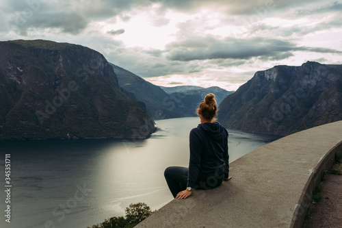 girl sitting on the edge of the parapet against the background of the mountains of Norway