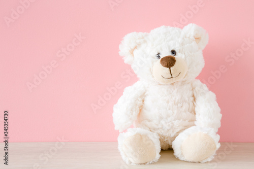 Obraz na płótnie Smiling white teddy bear sitting on table at pastel pink wall background