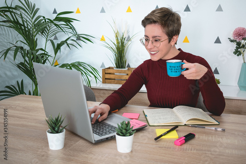 Woman with a coffee in hand teleworking at a desk with a laptop and a notebook
 photo