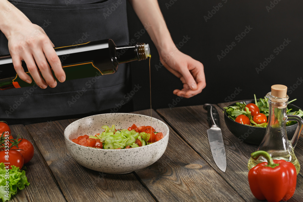 Woman cooking healthy food on wooden table with copyspace. Female hands adding olive oil into bowl with vegetable salad.