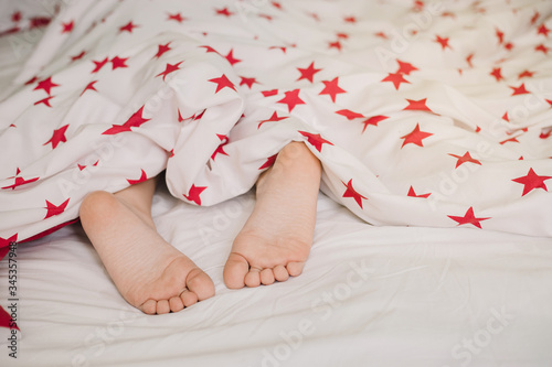 Feet of kid under white blanket with stars side view. Beautiful children's feet on the bed.
