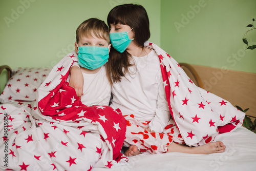 Sick boy and girl in medical masks are on duty under the covers. Sick child with fever and illness in bed. Corona virus