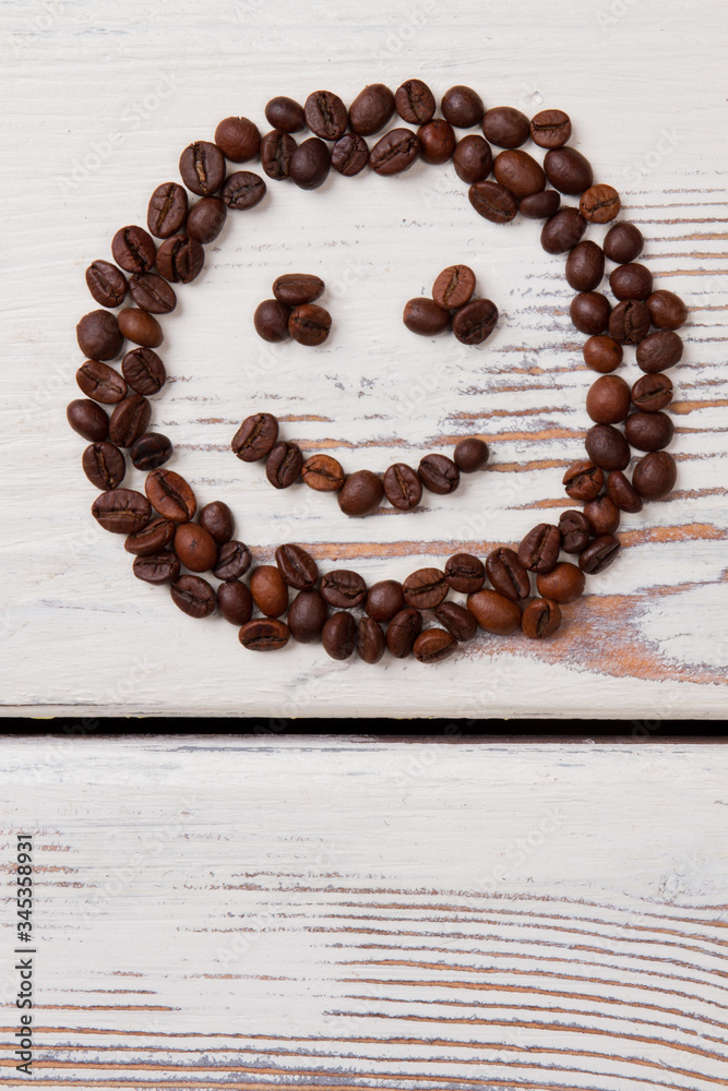 Coffee beans arranged in a smiling face. Brown seeds on white wood. Coffee beans arranged in a smiling face. Brown seeds on white wood.
