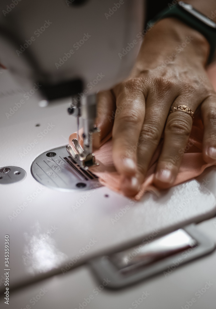 closeup a seamstress's hand with a gold ring on her finger that sews a piece of pink chiffon fabric using a sewing machine, closeup a seamstress's hand with a gold ring on her finger that sews a piece of pink chiffon fabric using a sewing machine,