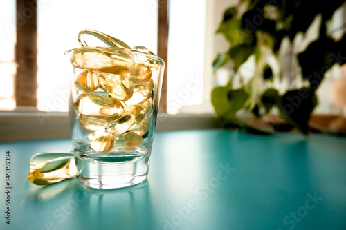 A glass cup with omega 3 vitamins stands on a blue table near the window, near a birch tree,.