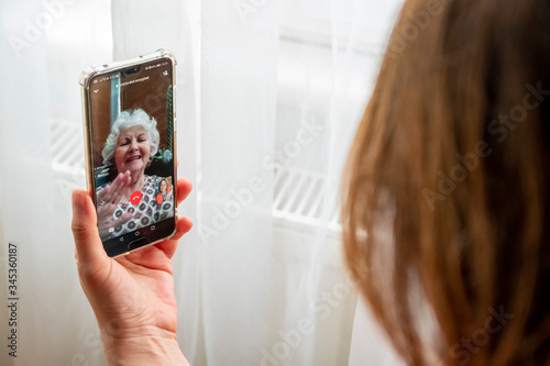 Mother's day concept: Because of lockdown mother and daughter are chatting online with video call and celebrating. Lady with white hair visibel on screen waves her hand photo